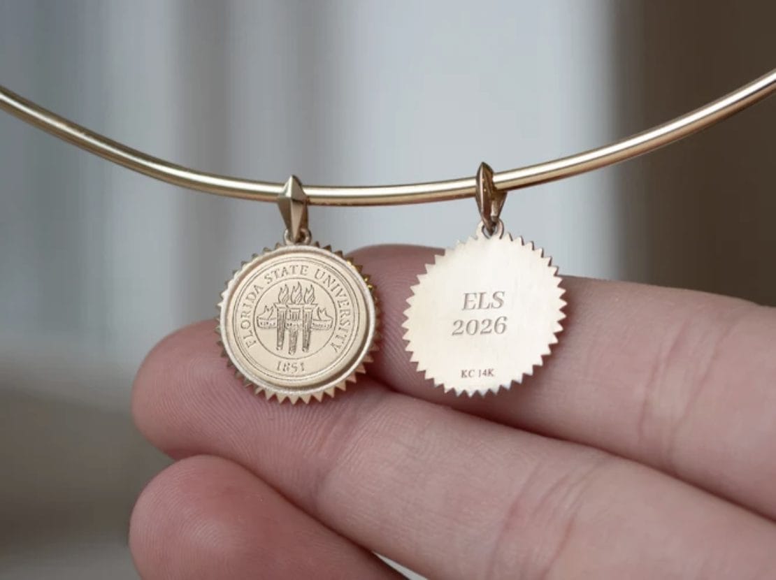 Dos colgantes dorados de Kyle Cavan en una pulsera, sostenidos en una mano